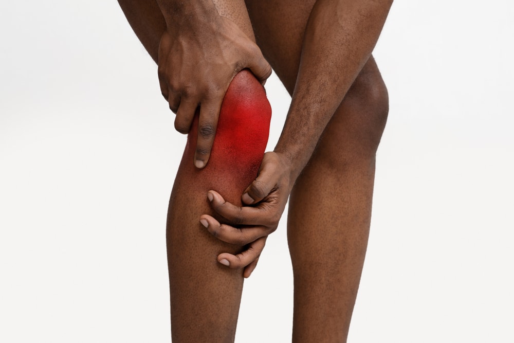 A man hold suffering from chronic joint pain holds his knee in discomfort.